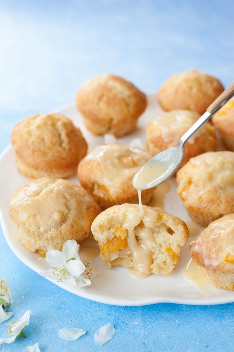 passion fruit glaze is being drizzled over mango muffins