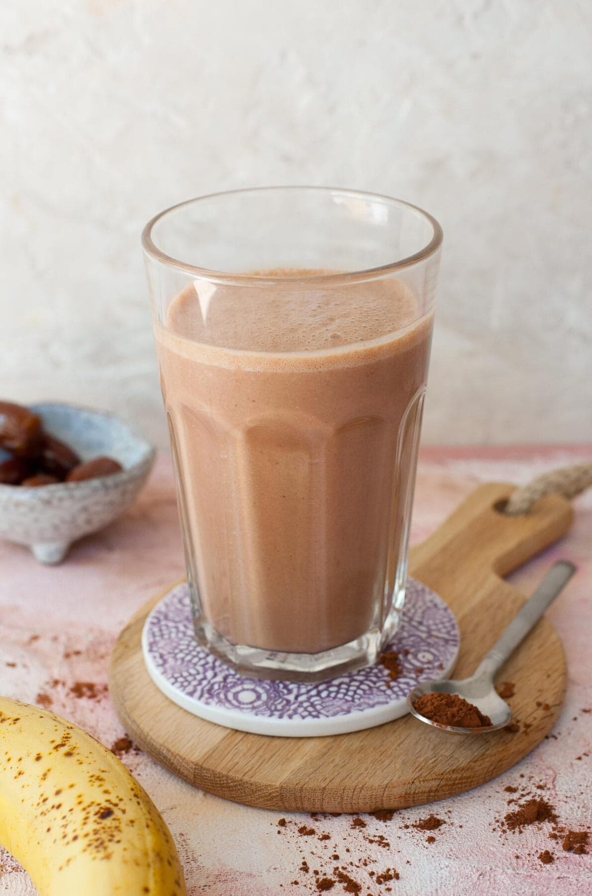 Chocolate peanut butter banana smoothie in a high glass, cocoa powder and bananas in the background