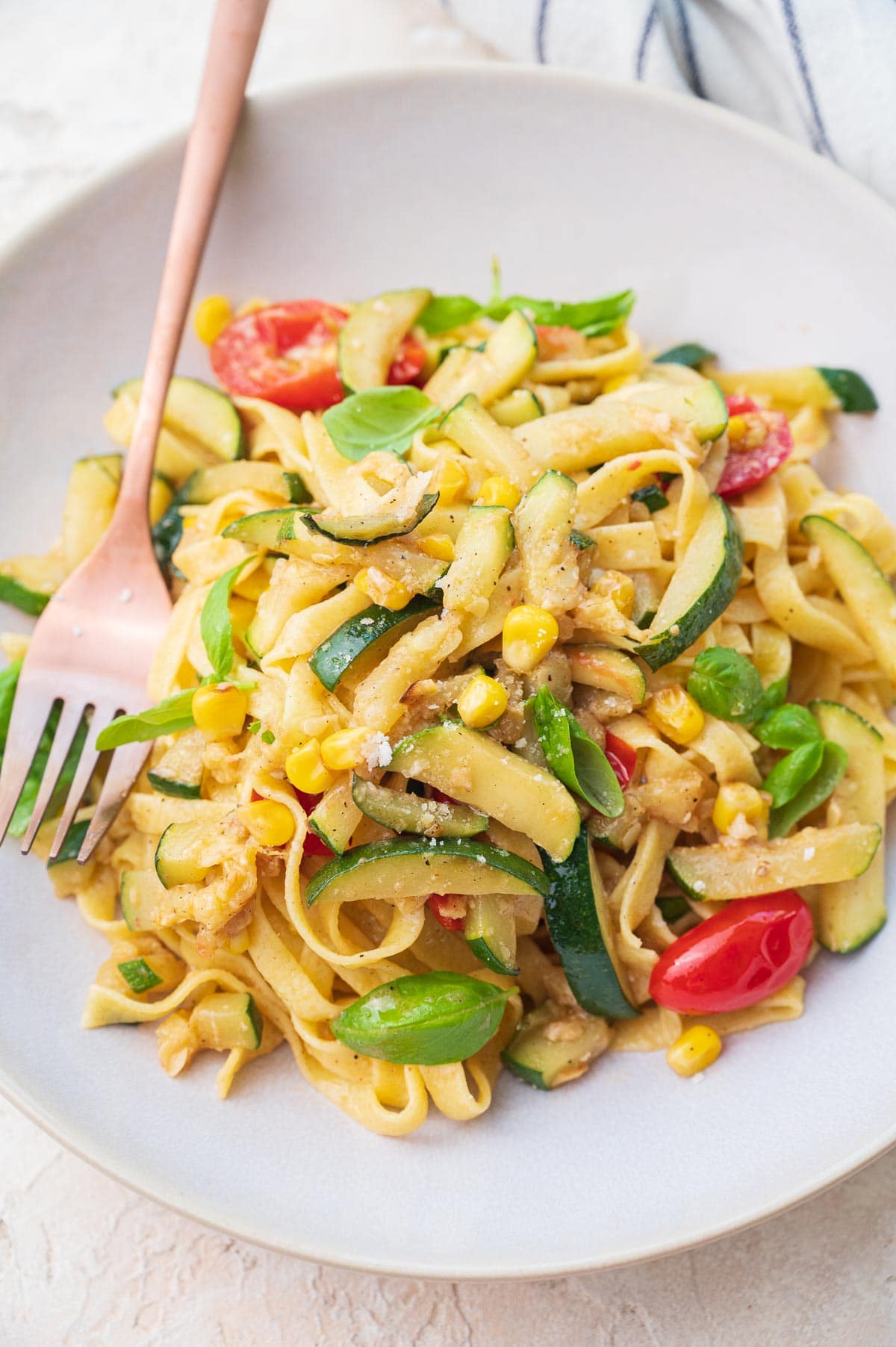 Zucchini pasta with corn and tomatoes on a beige plate.