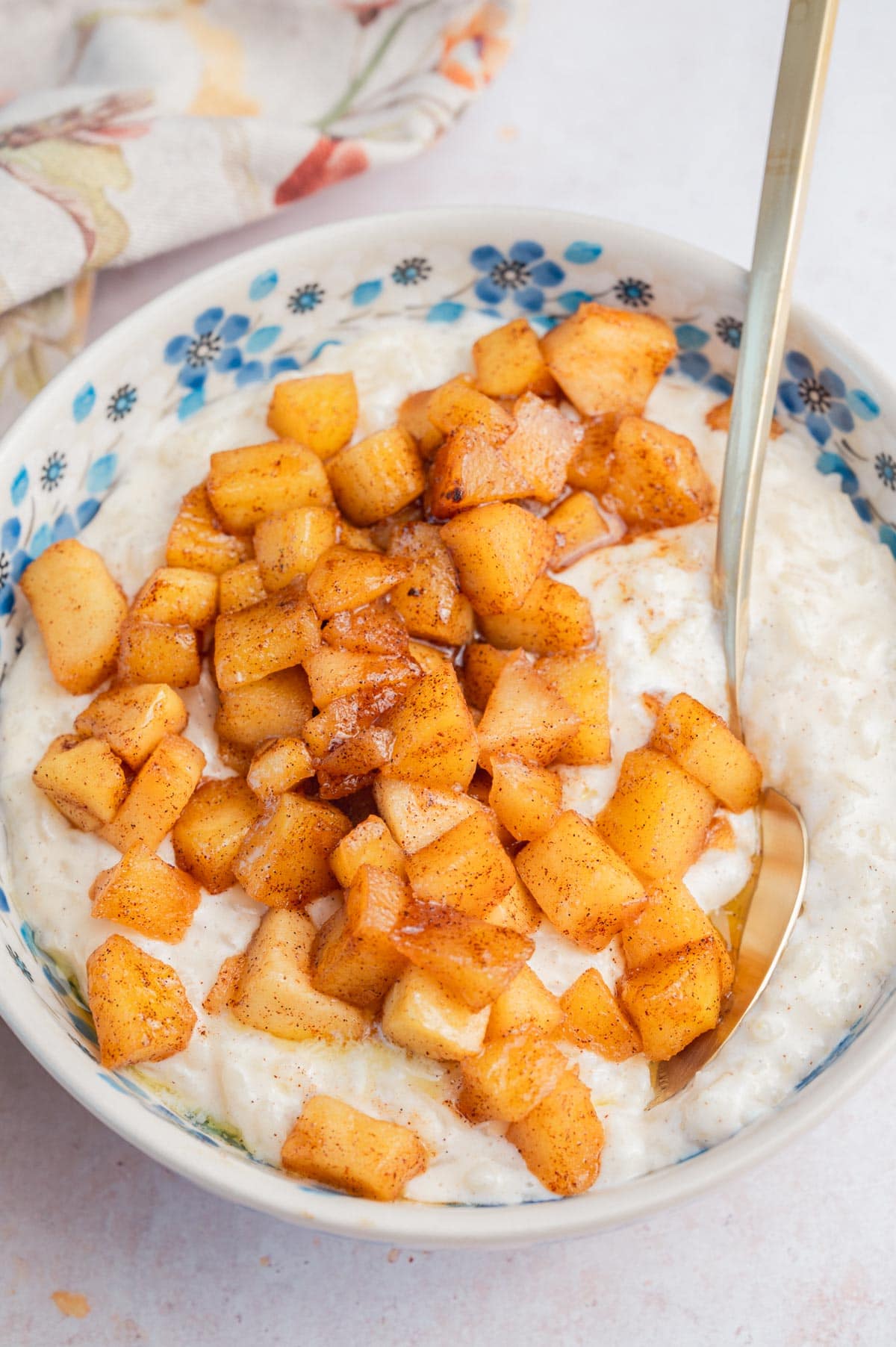 Milchreis in a white bowl topped with sauteed cinnamon apples.